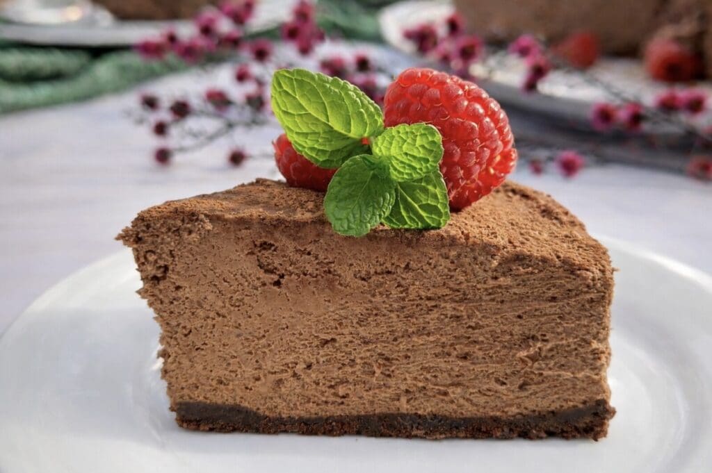 A side view of a slice of the Chocolate Mousse Cake looking creamy and rich, topped with a mint leaves and raspberries