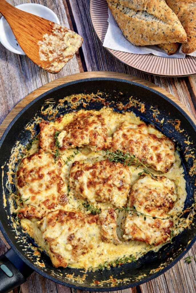 Creamy cheesy chicken thighs cooked in a skillet with a rich mustard sauce, garnished with fresh thyme and served with crusty bread on the side.