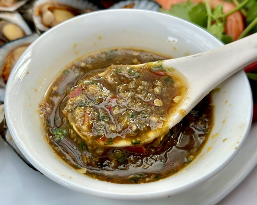 Close up of Thai Nam Jim sauce showing its chunky texture with garlic, chilli and fresh herbs.