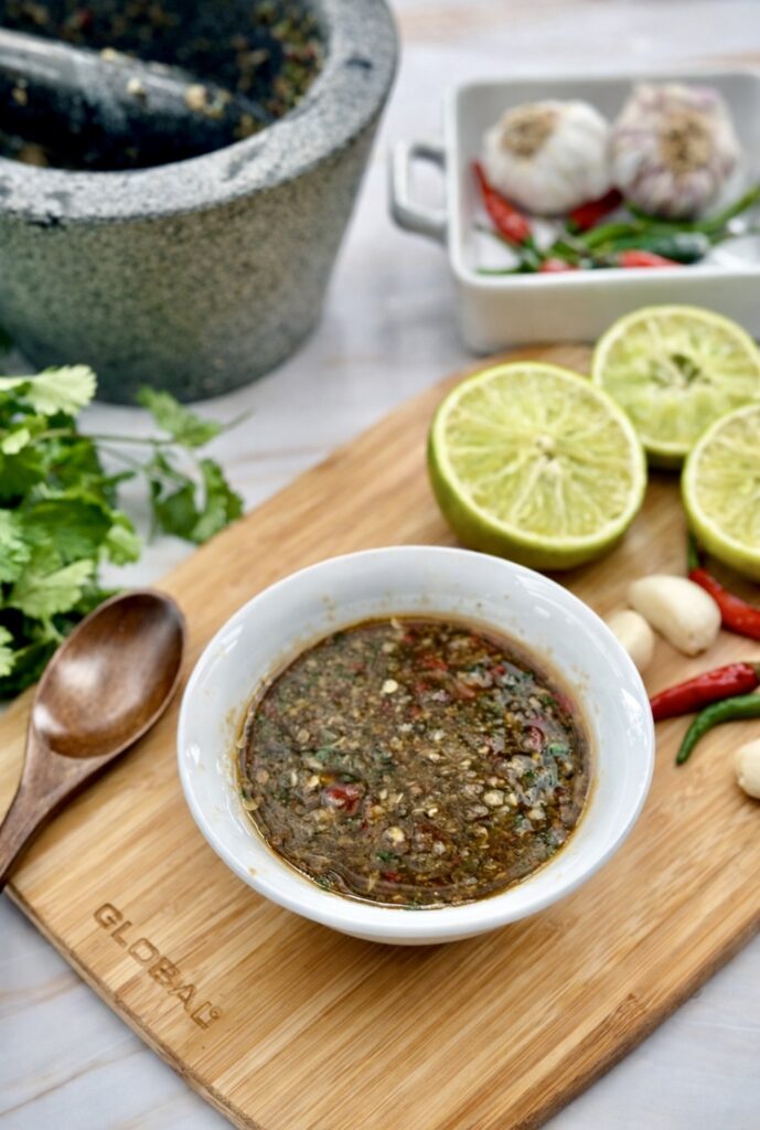 Thai Nam Jim sauce in a small bowl next to cooked prawns and shellfish, garnished with fresh coriander and lime.