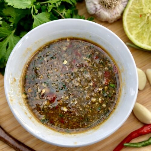 Top view of Thai Nam Jim sauce on a wooden board with coriander, garlic, red and green chillies and sliced lime.