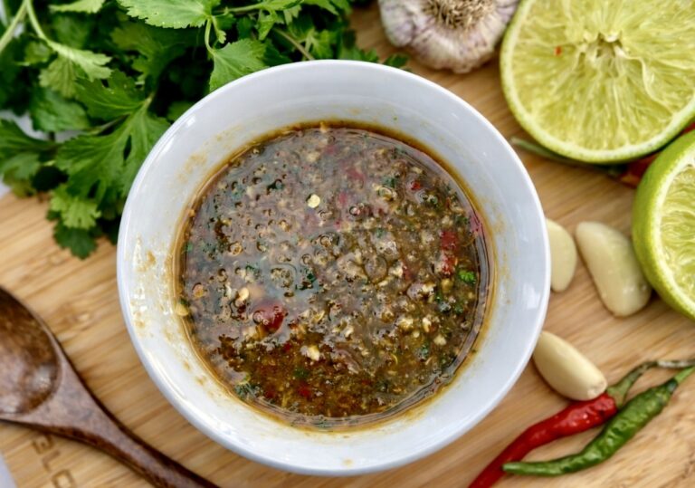Top view of Thai Nam Jim sauce on a wooden board with coriander, garlic, red and green chillies and sliced lime.