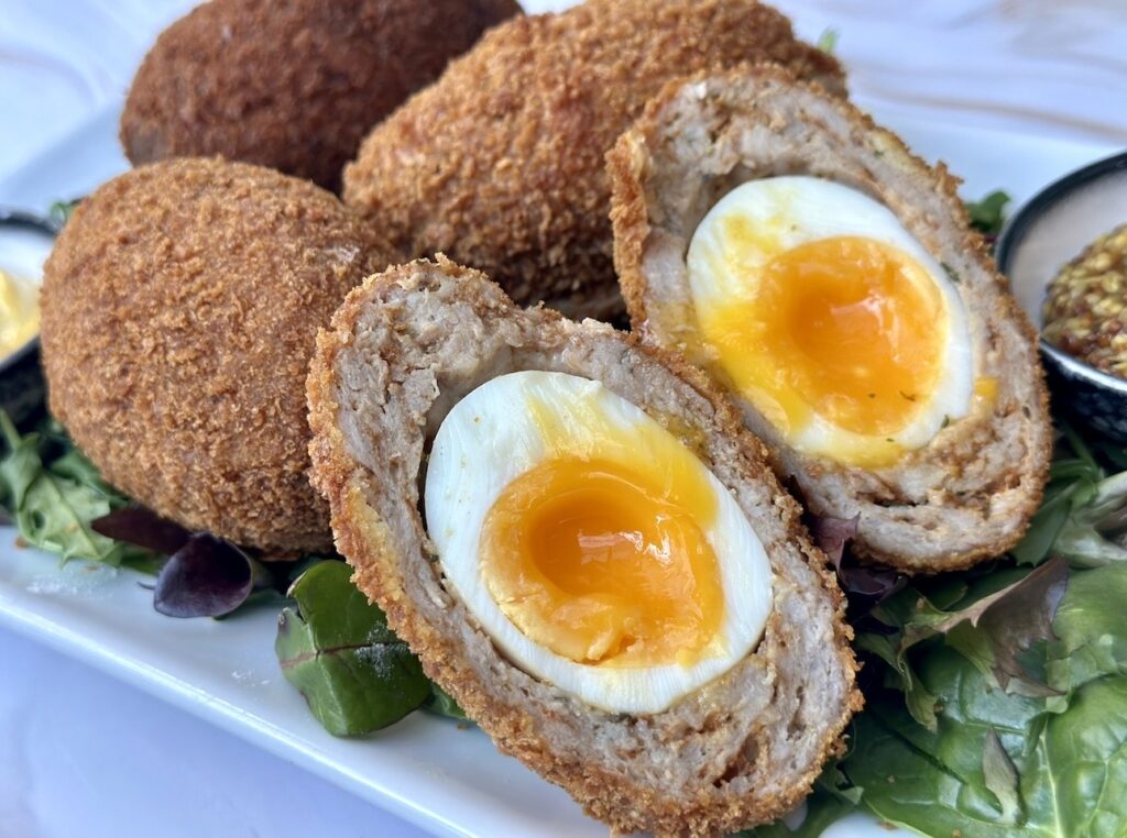 Close up of Scotch eggs sliced open to reveal jammy egg yolks, wrapped in seasoned sausage meat and crispy breadcrumb coating