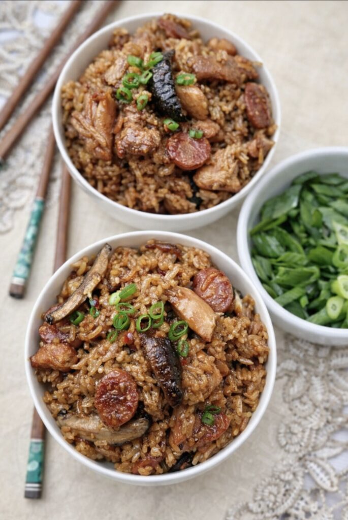 Rice cooker claypot chicken rice with lap cheong sausage, shiitake mushrooms and fluffy seasoned rice in white bowls

