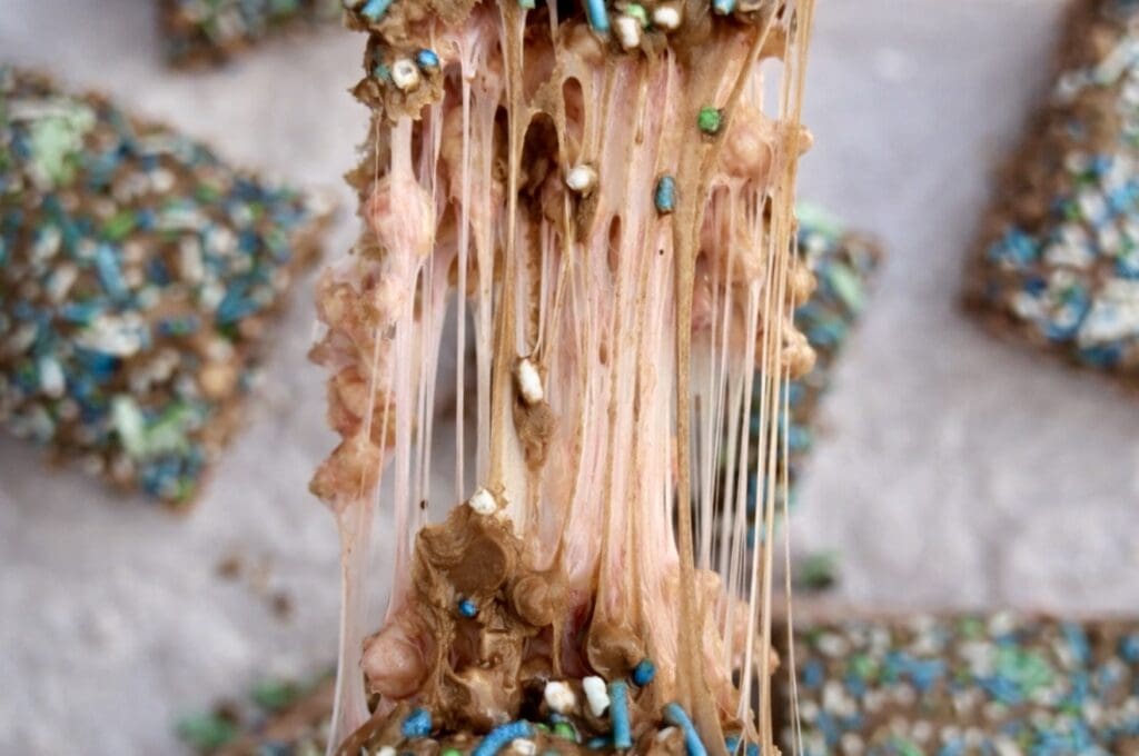 Gooey rice bubble slice being pulled apart, showing stretchy marshmallow and melted chocolate