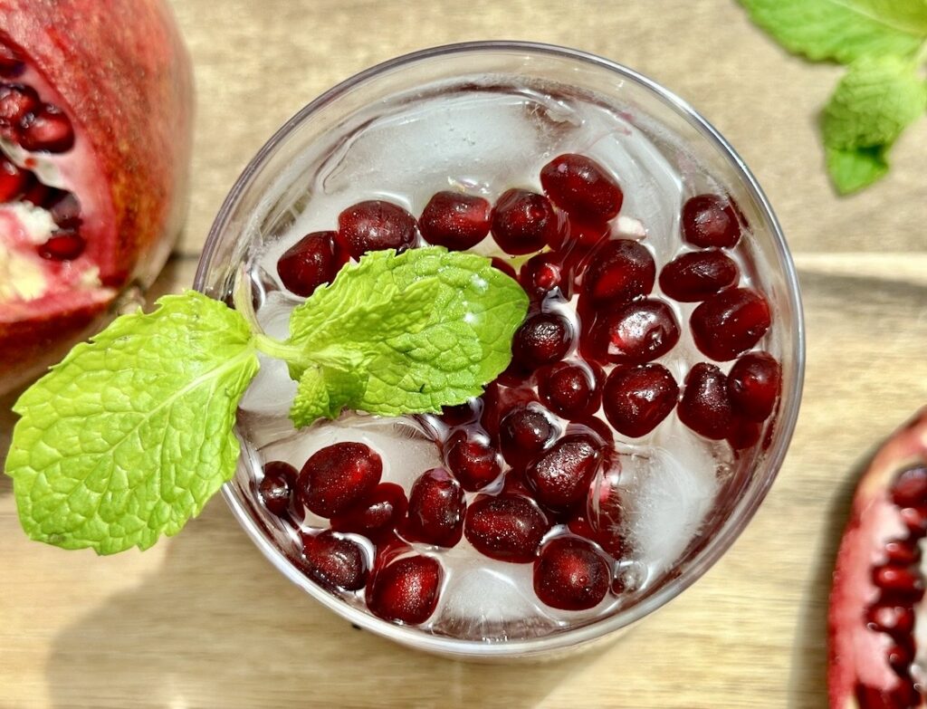 Pomegranate cocktail served over ice with lime wedges and pomegranate arils