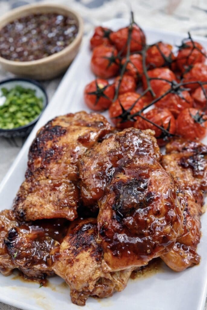 Juicy balsamic chicken cooked until golden and caramelised, paired with roasted vine tomatoes on a white platter.