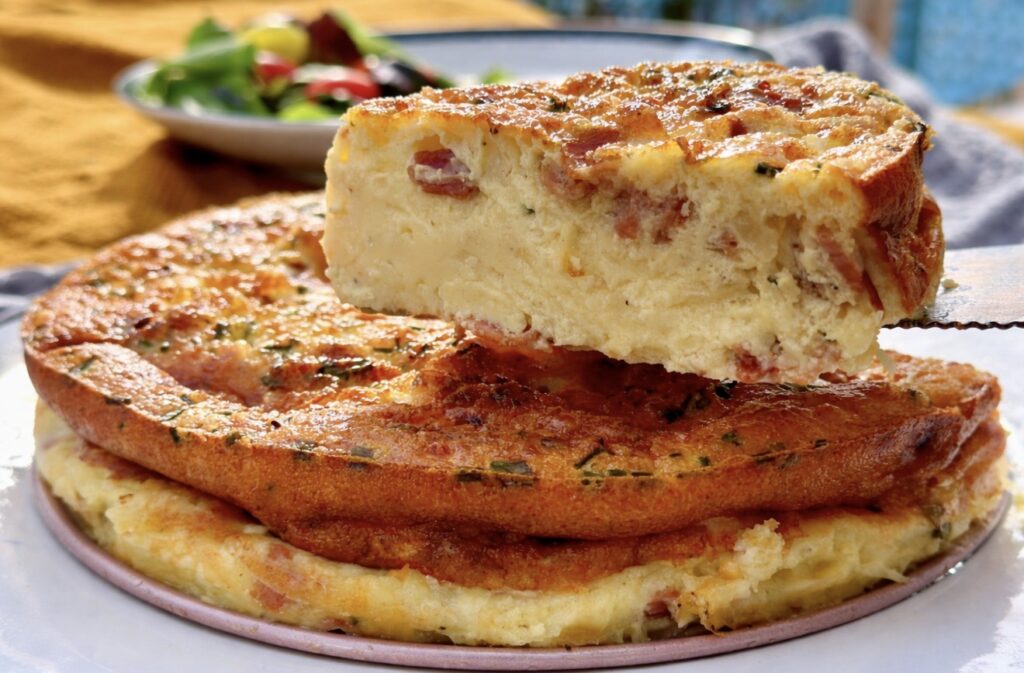 A cut slice of bacon and cheese crustless quiche held up, showing the custard-like texture