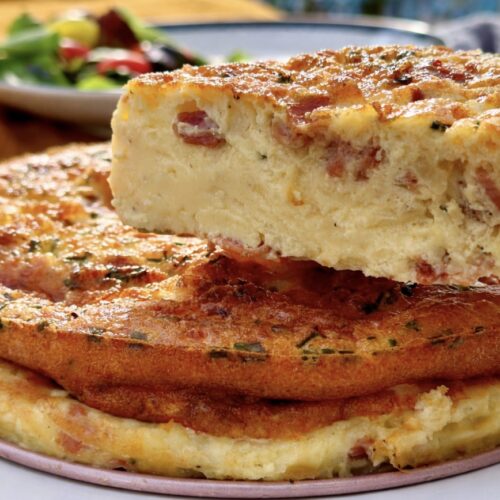 A cut slice of bacon and cheese crustless quiche held up, showing the custard-like texture