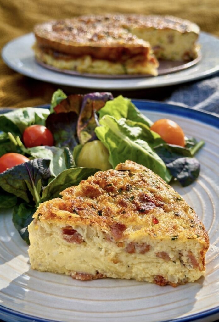 Slice of Crustless Quiche with Bacon and Cheese served with the whole quiche in the background