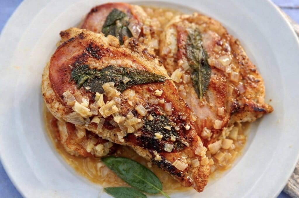 Chicken saltimbocca with prosciutto and sage served in a light garlic and onion sauce on a white plate