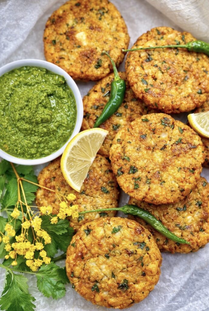 Crispy Indian aloo tikki potato patties arranged with vibrant green chutney, coriander leaves, green chillies, and lemon wedges.