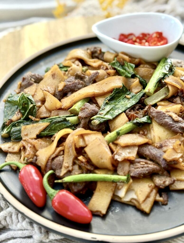 Homemade pad see ew featuring stir fried beef, wide rice noodles and Chinese broccoli, garnished with fresh chilli