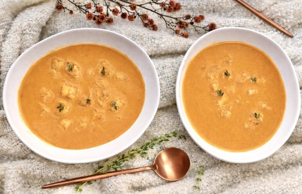 Rich and creamy prawn bisque with chunks of prawns, garnished with thyme in white bowls