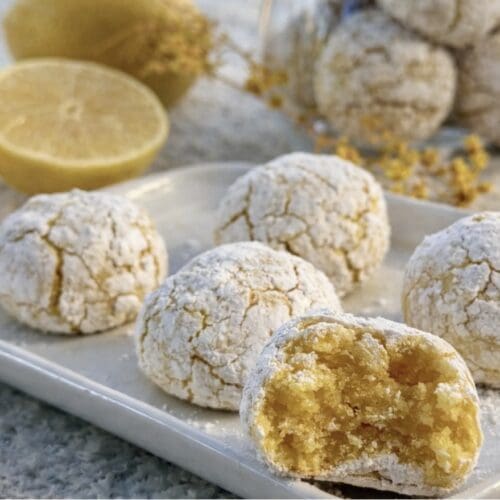 Crispy chewy Lemon Amaretti cookies on a plate with one bitten showing the inside