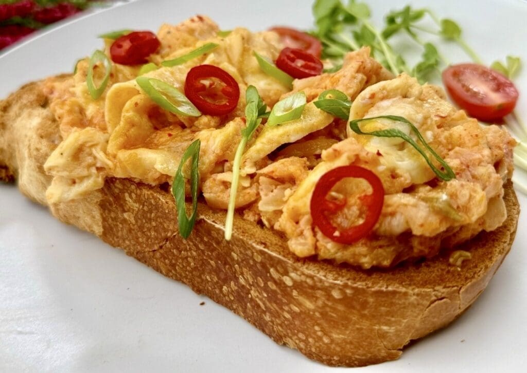Cheesy kimchi scrambled eggs on toast, garnished with fresh spring onions and red chilli slices