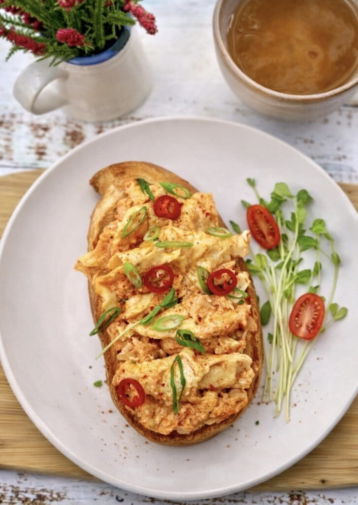 Spicy kimchi scrambled eggs with cheese on toasted bread, photographed overhead on a white plate