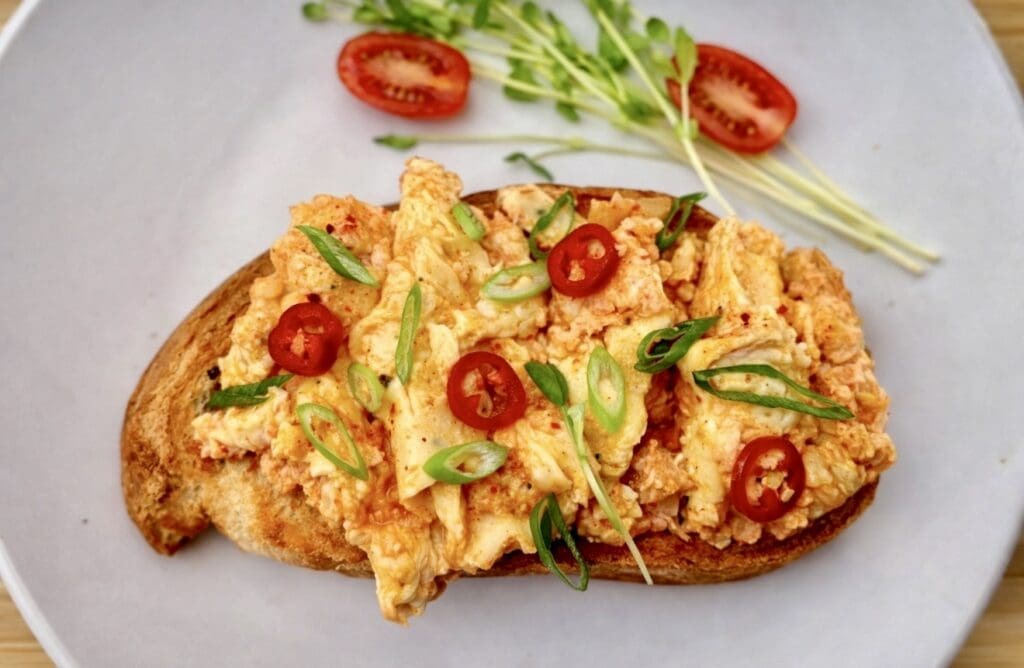 Kimchi scrambled eggs with melted cheese served on toasted sourdough, topped with sliced chilli and spring onions