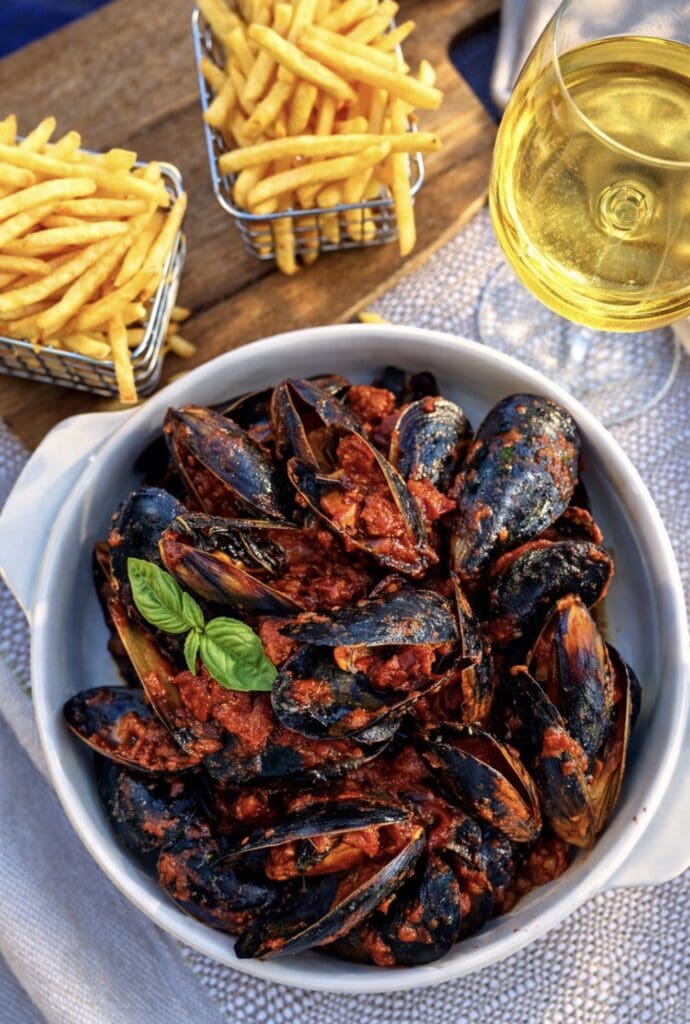 Close-up of mussels cooked in a rich spicy tomato and chorizo sauce, served in a white bowl