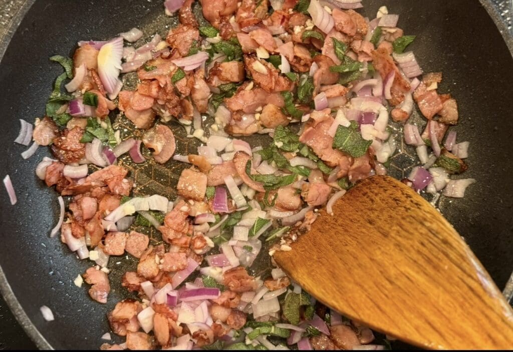 Adding the garlic, onions and sage with the bacon into the pan