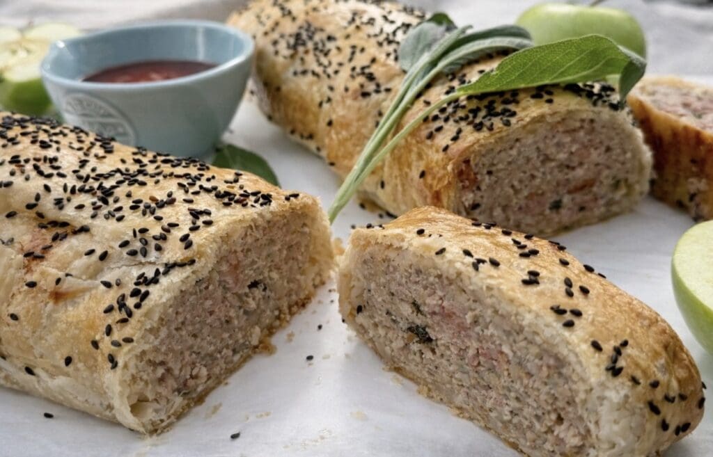 Sliced pork and apple sausae rolls up close with tomato sauce and sage leaves