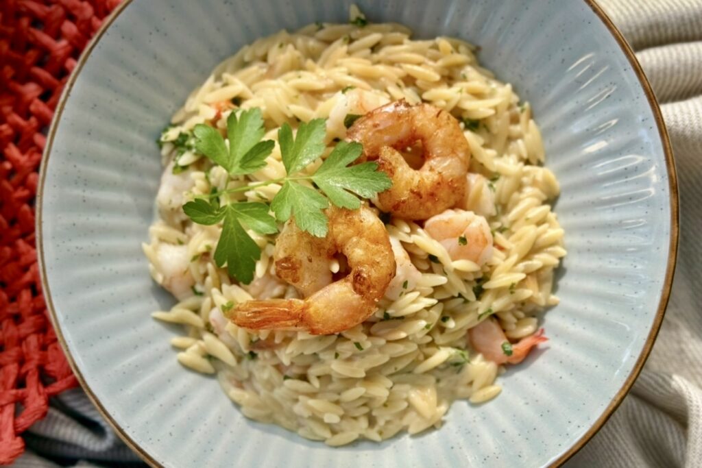 Top view of creamy garlic shrimp orzo in a ceramic bowl garnished with parsley and pan-seared prawns