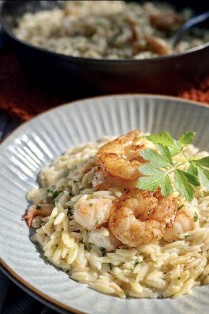 Creamy shrimp orzo pasta with garlic butter prawns served in a blue bowl with natural light and fresh parsley garnish