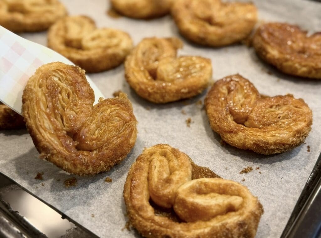 Golden palmiers on a baking tray being flipped over with spatula