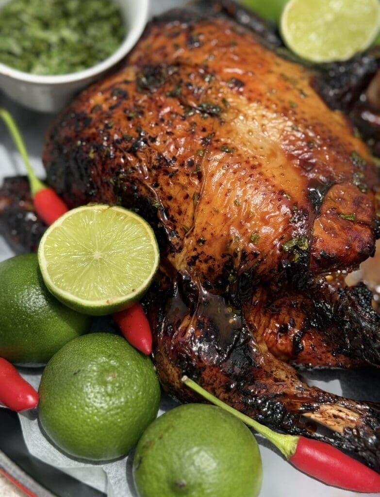 Close-up of whole roast chilli lime chicken with crispy skin, fresh limes and red chillies