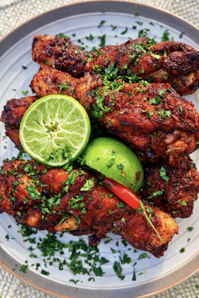 An overhead shot of a large plate of Thai Red Curry Roast Chicken drumsticks garnished with lemon, chillies and coriander