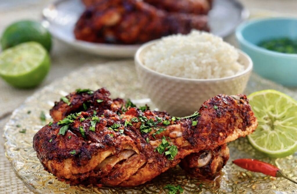 A close up of Thai Red Curry Roast Chicken drumstick covered in dark red spices served with a bowl of rice