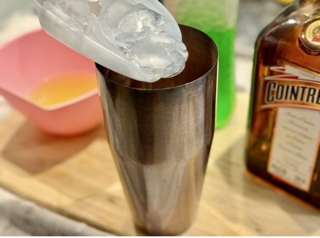 A large scoop of ice going into the cocktail shaker