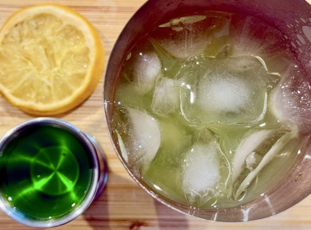 Top view showing shaker with ice and Midori next next to it, ready to shake and make Japanese Slipper Cocktail 