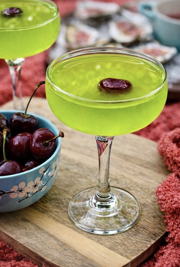 Bright green Japanese Slipper Cocktail in a coupe glass with cherry garnish and fresh cherries