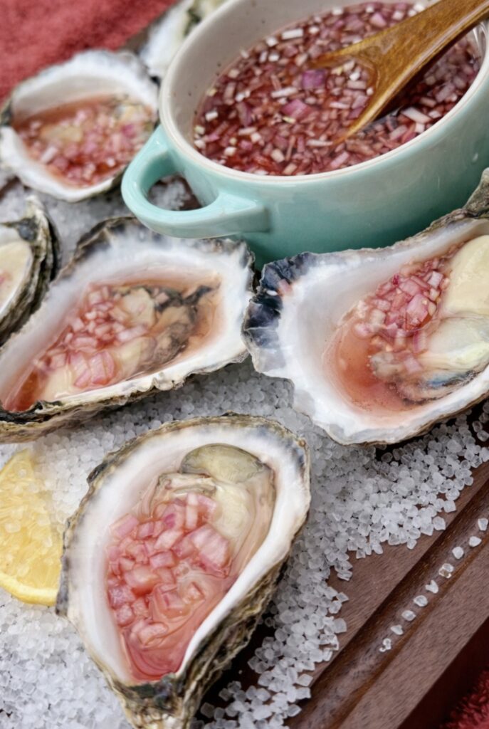 Mignonette Sauce For Oysters served alongside freshly shucked oysters arranged on coarse rock salt