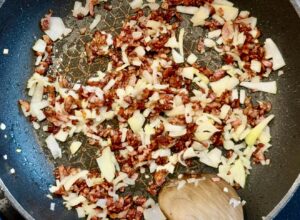 Bacon and onion sautéing in a frying pan with garlic for creamy bacon and onion dip recipe