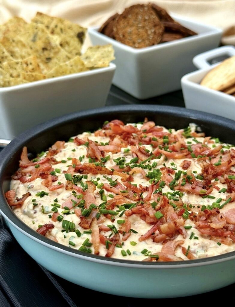 Homemade creamy bacon and onion dip garnished with bacon and chives, photographed as a party snack with crackers