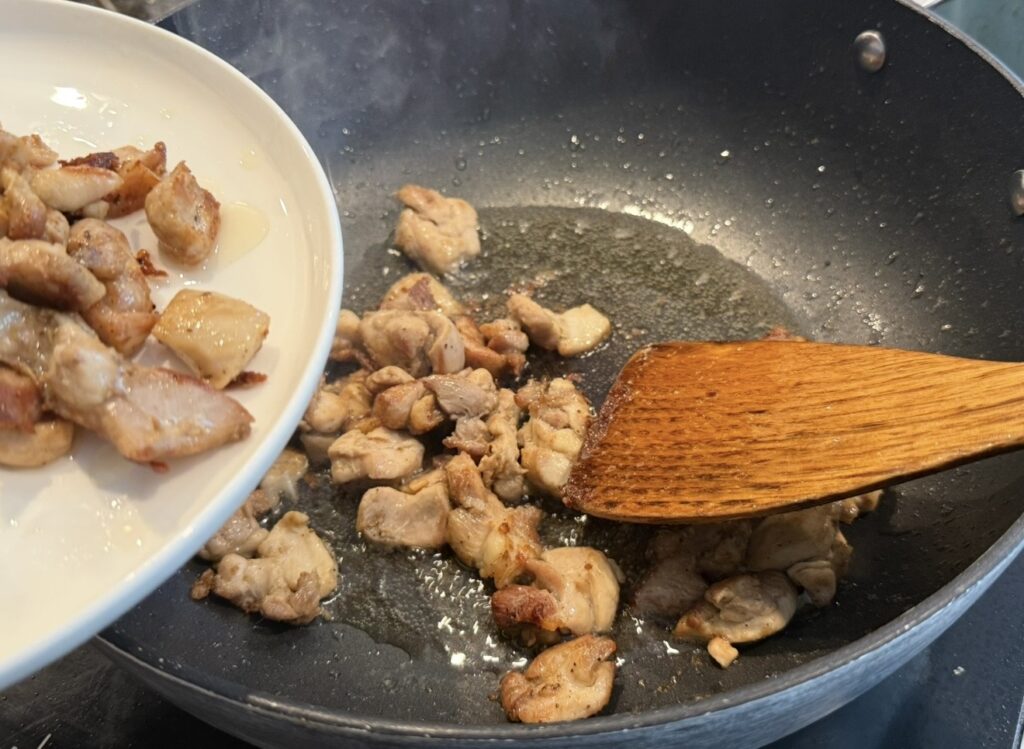 Removing the browned chicken pieces onto a plate before making the honey sambal sauce