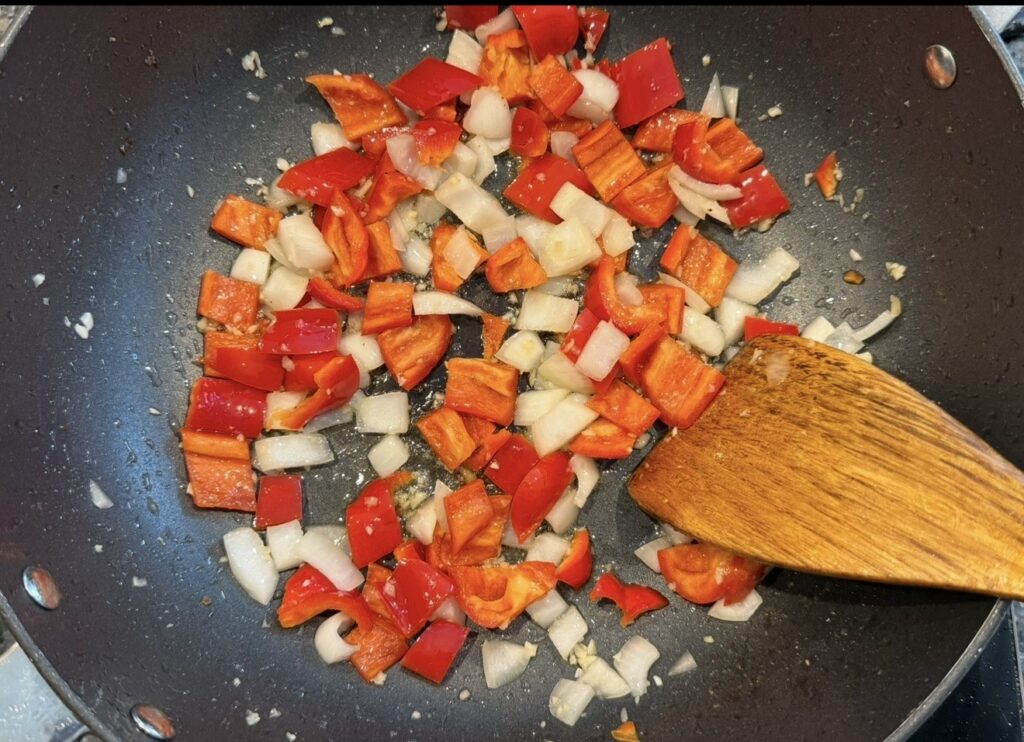 Diced onion and red capsicum sautéing in a pan as the base for honey sambal chicken