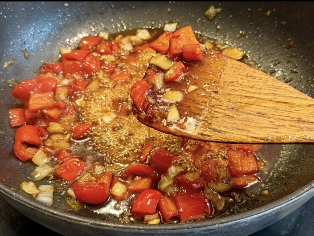 Honey sambal sauce simmering in a pan with chicken and capsicum, becoming thick and glossy