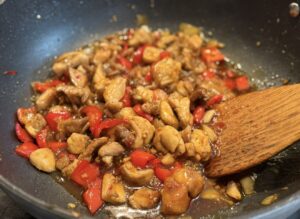 Chicken pieces browning in a pan with red capsicum as the honey sambal sauce begins to caramelise