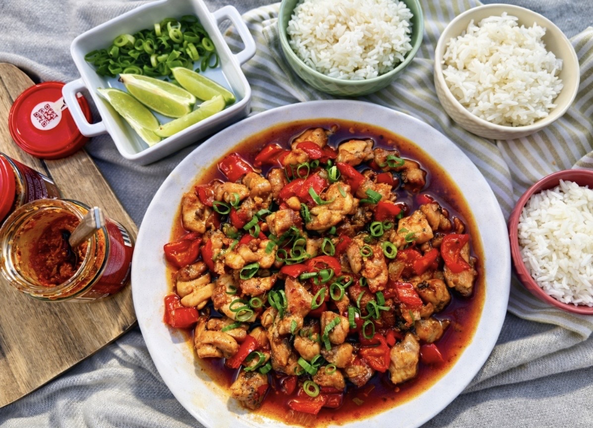 Overhead view of honey sambal chicken with sticky sauce, red capsicum and spring onion garnish, served with rice