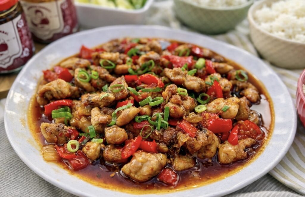Honey sambal chicken served on a white plate with red capsicum, spring onions and a glossy sweet and spicy sauce