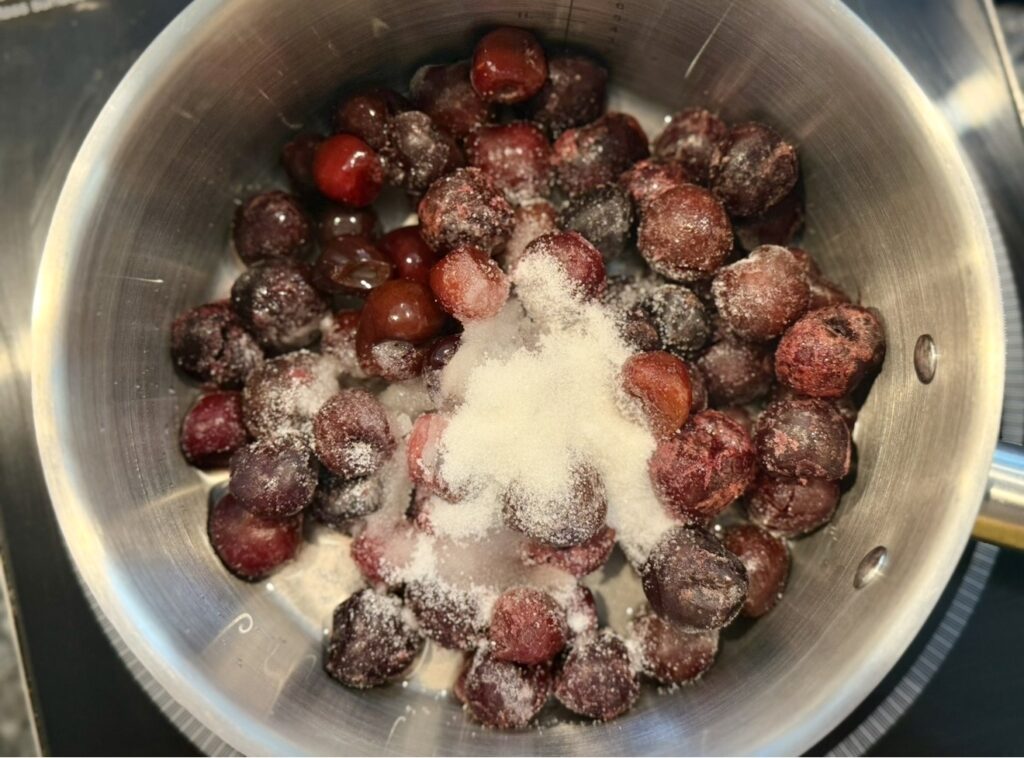 Frozen cherries in a saucepan with sugar and water