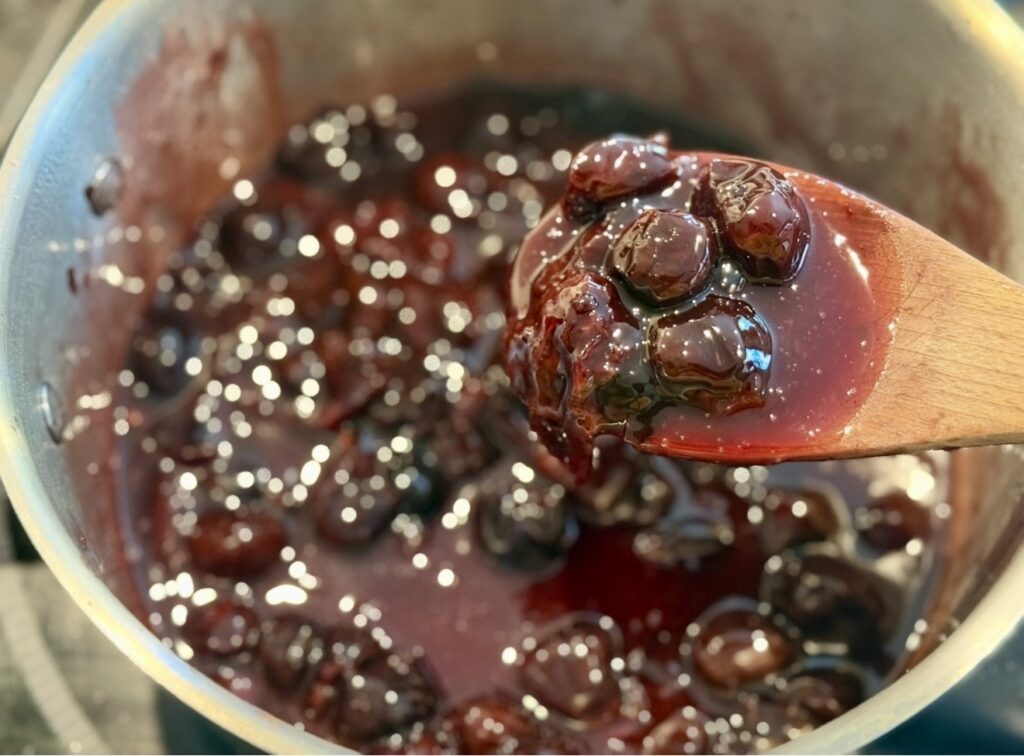 lifting the cherries with a wooden spoon to examine the texture and thickness of sauce