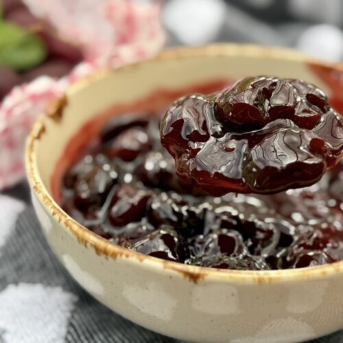 Close-up of glossy homemade cherry compote with whole cherries in a ceramic bowl.
