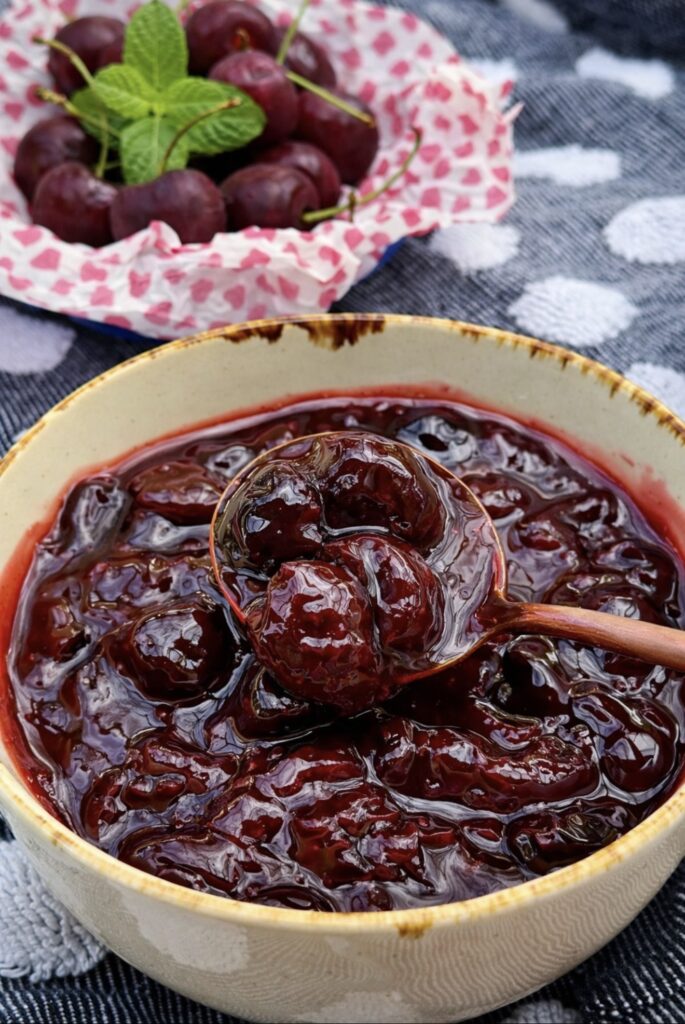 Cherry compote slowly dripping from a spoon back into a bowl, showing its thick consistency.